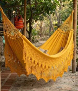 Hamaca artesanal de Morroa color amarillo instalada en un jardín con flecos de macramé tejidos a mano