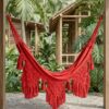 Hamaca de Morroa con macramé color rojo instalada en un jardín tropical