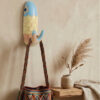 Perchero de pez Escamas en ambiente decorativo Perchero artesanal de pez con diseño Escamas usado como perchero decorativo para colgar un bolso tejido en una pared interior.
