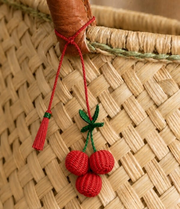 Charm artesanal de cereza decorando un bolso Charm para bolso de fruta en palma de iraca colocado en un bolso tejido