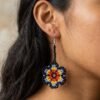 Modelo luciendo aretes de chaquiras Kamentsa en forma de flor multicolor tejida a mano.