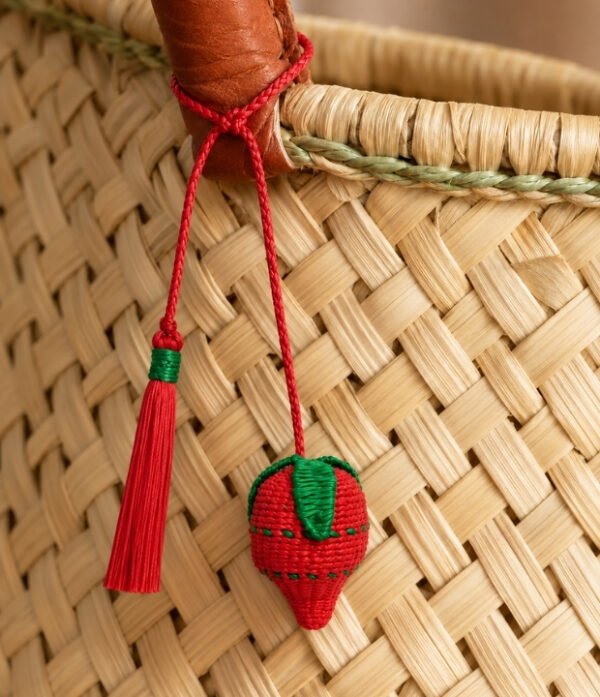 Charm artesanal de fresa decorando un bolso Charm para bolso de fruta en palma de iraca colocado en un bolso tejido