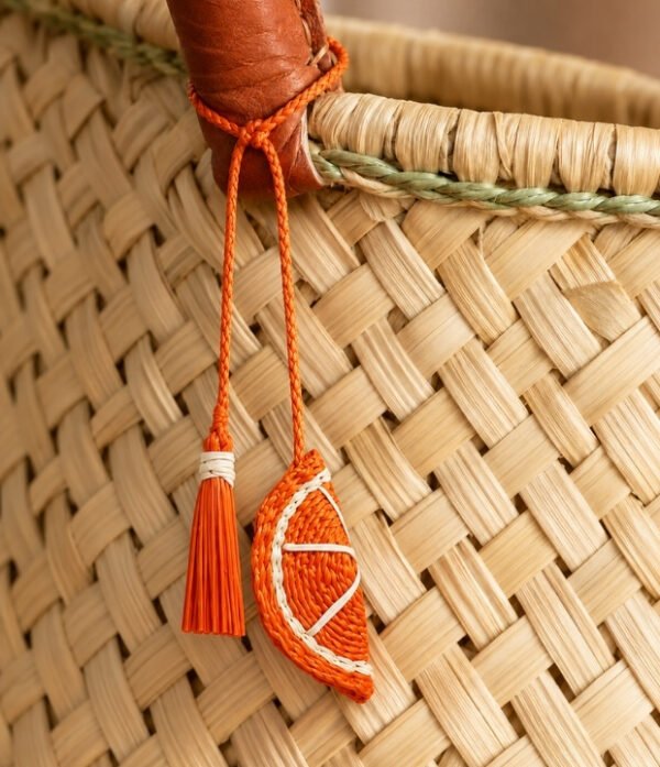 Charm artesanal de naranja decorando un bolso Charm para bolso de fruta en palma de iraca colocado en un bolso tejido