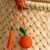 Charm artesanal de naranja decorando un bolso Charm para bolso de fruta en palma de iraca colocado en un bolso tejido