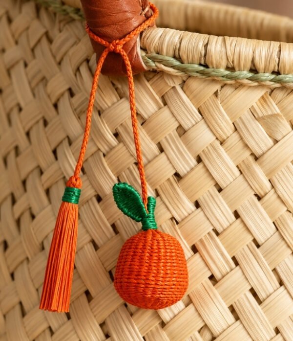 Charm artesanal de naranja decorando un bolso Charm para bolso de fruta en palma de iraca colocado en un bolso tejido