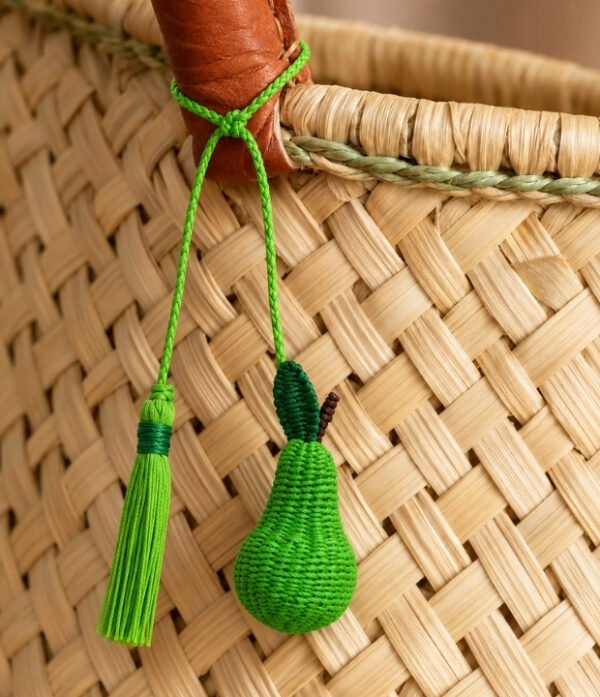 Charm artesanal de pera decorando un bolso Charm para bolso de fruta en palma de iraca colocado en un bolso tejido