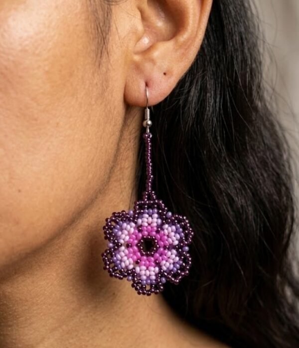 Primer plano de modelo luciendo aretes de chaquiras Kamentsa rosados en forma de flor.