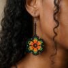 Modelo luciendo aretes de chaquiras Kamentsa verdes con detalles naranjas hechos a mano.