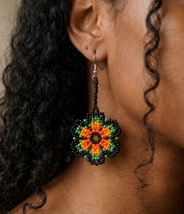 Modelo luciendo aretes de chaquiras Kamentsa verdes con detalles naranjas hechos a mano.